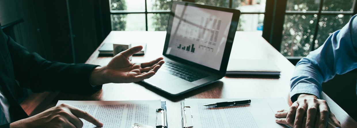 Klant bespreekt bij een medewerker van een bank zijn krediet mogelijkheden achter een bureau met papieren en een laptop