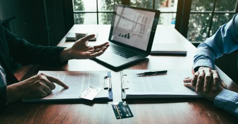 Klant bespreekt bij een medewerker van een bank zijn krediet mogelijkheden achter een bureau met papieren en een laptop